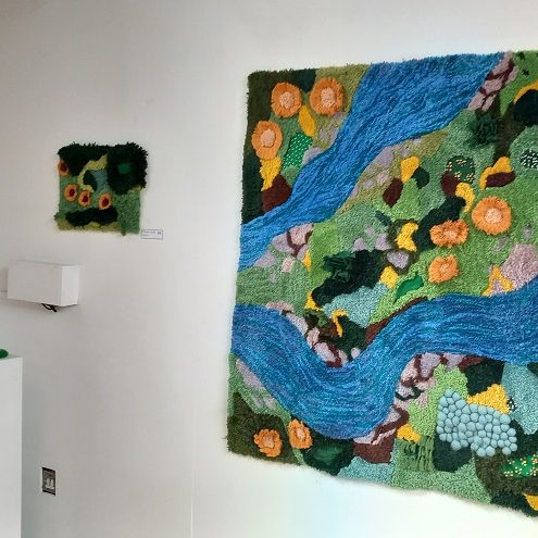 Photo of textile artwork hanging on white wall.  Artwork is abstract, blue and green.